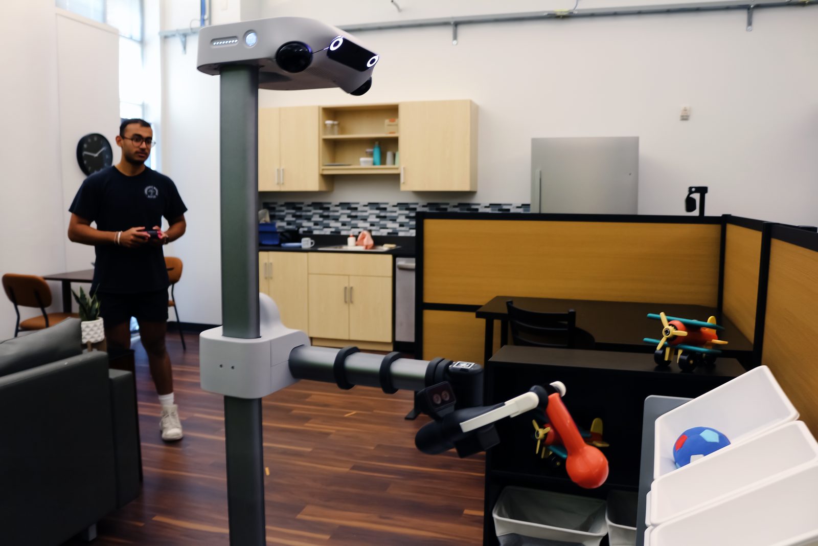 Ankit standing behind Stretch 4 as it holds a toy in the lab apartment